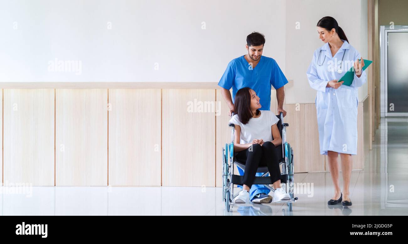 heureuse patiente asiatique souriante assise en fauteuil roulant avec une infirmière masculine parlant au médecin après avoir récupéré un plan de traitement chirurgical à l'hôpital Banque D'Images heureuse patiente asiatique souriante assise en fauteuil roulant avec une infirmière masculine parlant au médecin après avoir récupéré un plan de traitement chirurgical à l'hôpital Banque D'Images