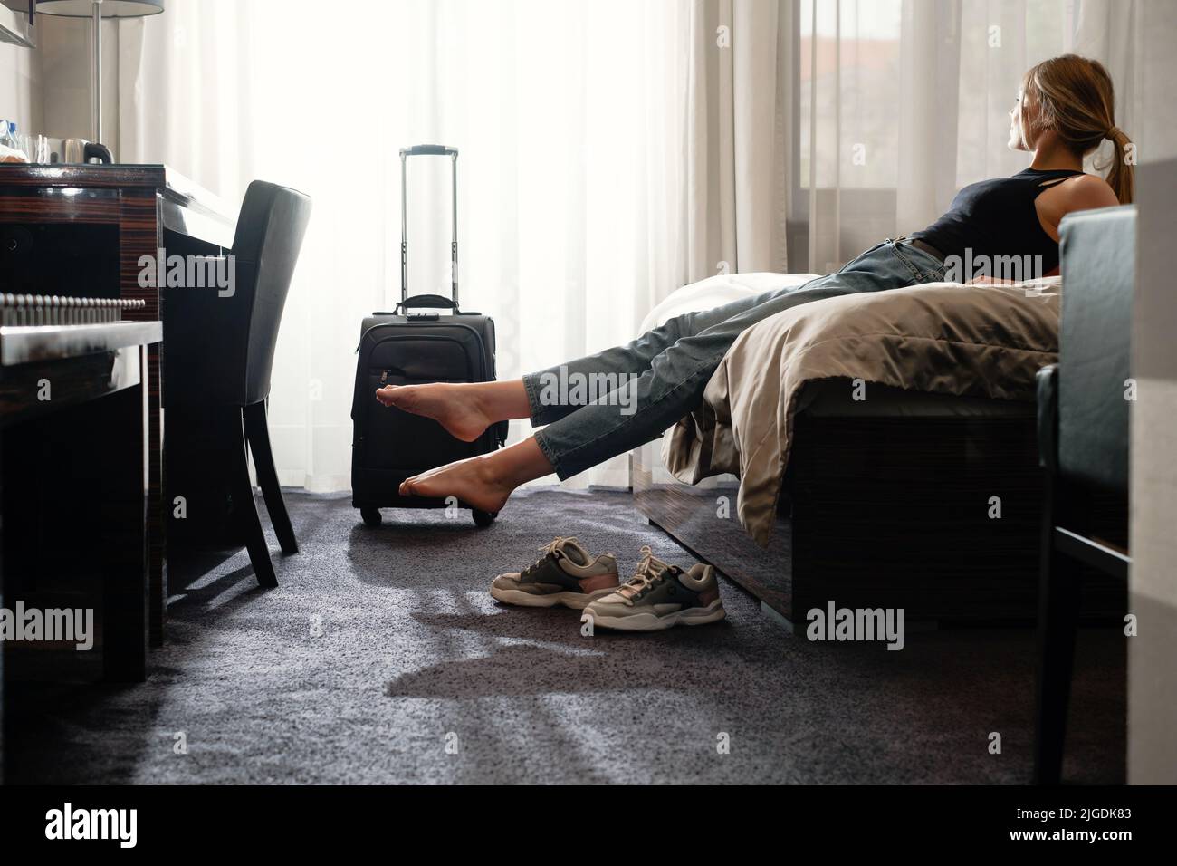 femme prenant des chaussures dans une chambre d'hôtel ensoleillée sur le lit. Touriste se détendre dans la chambre d'hôtel après avoir voyagé avec une valise. Bonne femme de se reposer Banque D'Images