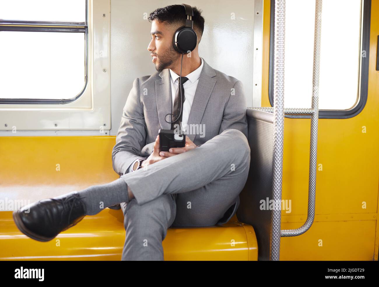 Les podcasts aident à passer le temps. Un jeune homme d'affaires portant des écouteurs et utilisant un téléphone portable tout en regardant par la fenêtre sur un train pendant son Banque D'Images
