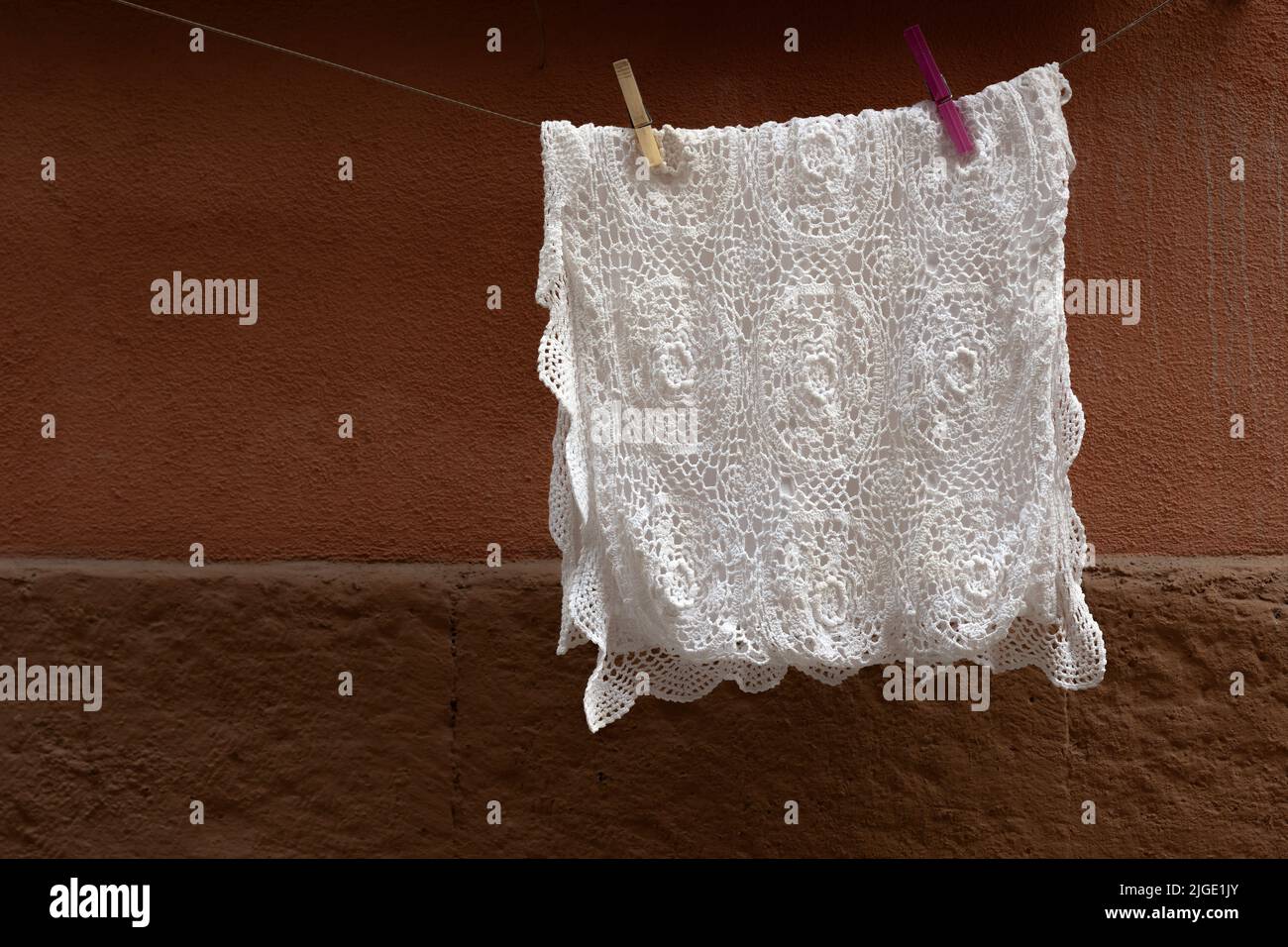 Nappe en crochet blanc, accrochée au fil pour suspendre, sécher après lavage. Arrière-plan avec paroi marron. Banque D'Images