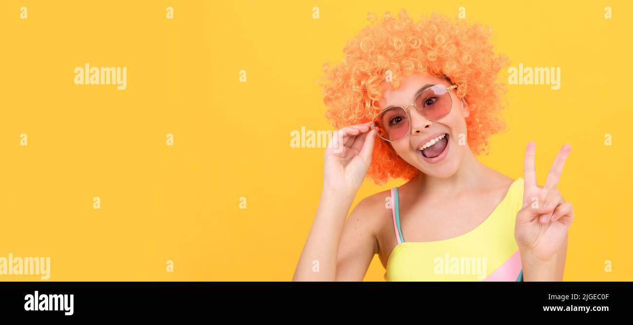 joyeux enfant dans des lunettes de soleil et un maillot de bain portant des cheveux de perruque orange montrant le geste de paix, la paix. Adolescent drôle sur la fête, affiche en-tête de bannière Banque D'Images