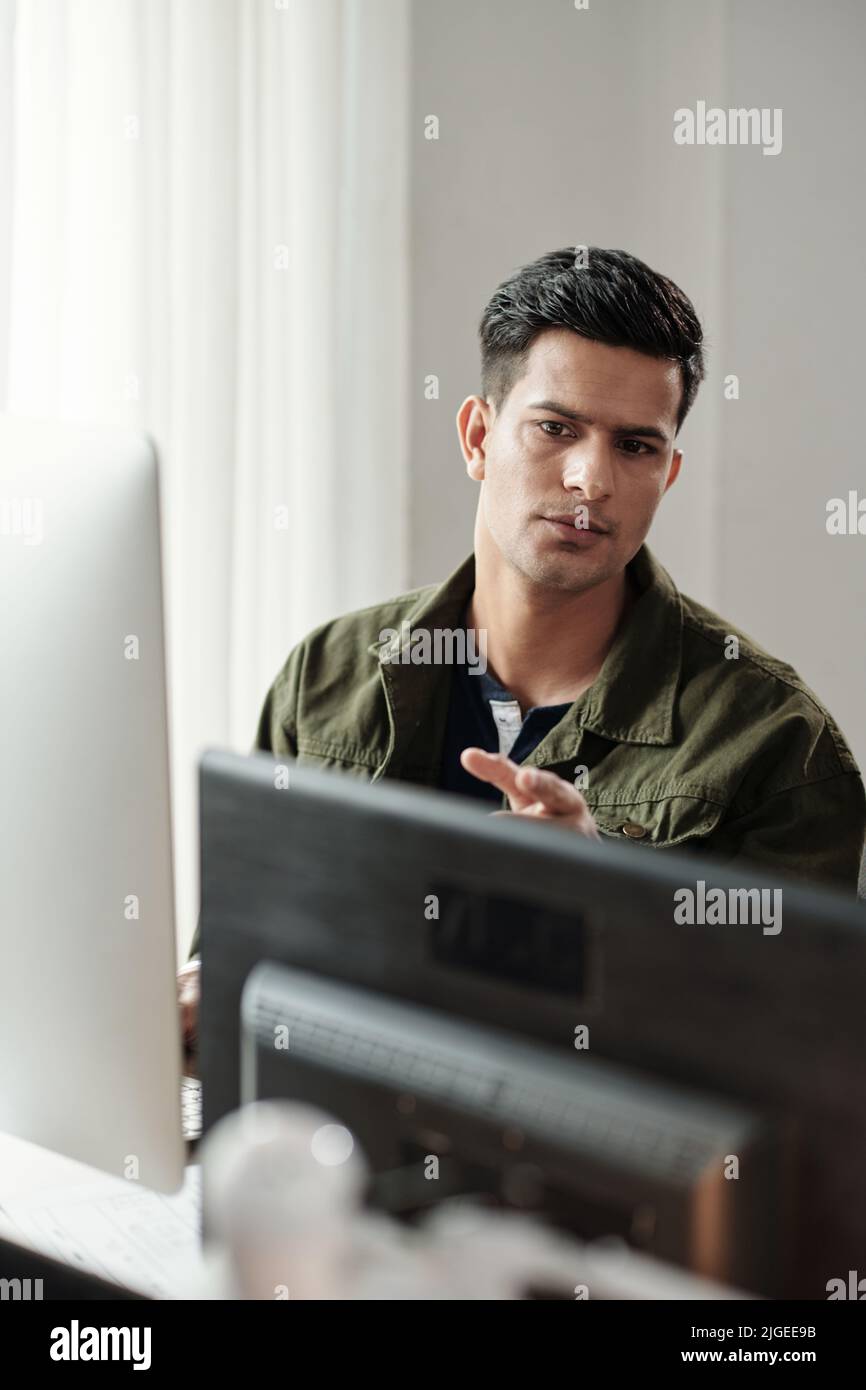 Un jeune programmeur indien sérieux vérifie le code sur deux écrans d'ordinateur sur son bureau Banque D'Images