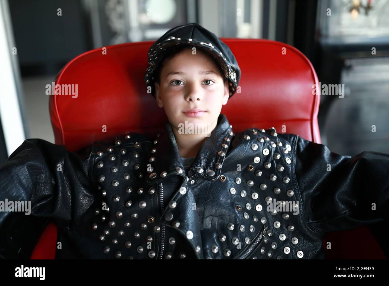Portrait de l'enfant dans une veste en cuir et une casquette assis sur une chaise Banque D'Images