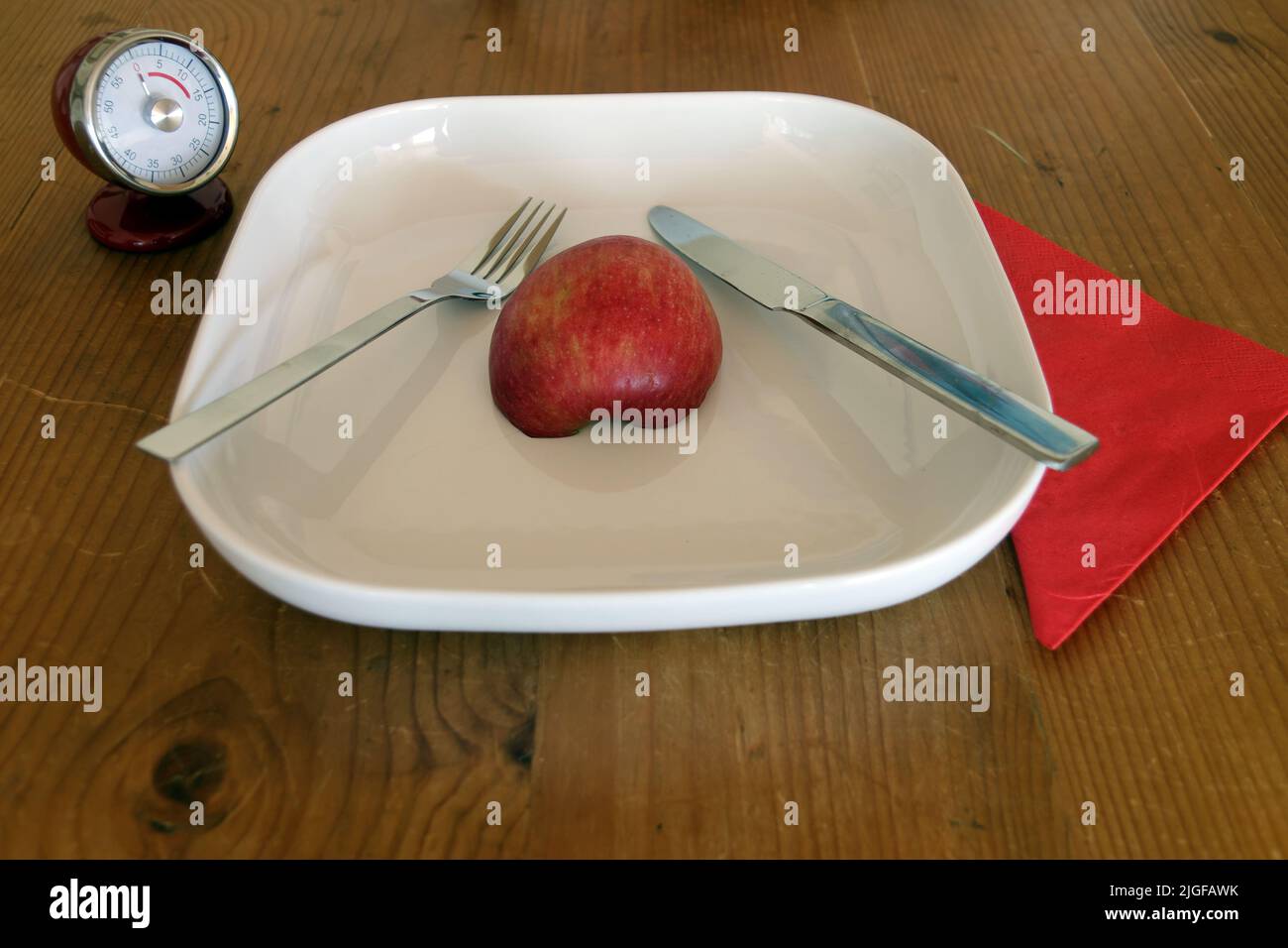 Image symbolique pour le contrôle du régime et du poids, jeûne intermittent : assiette avec demi-pomme, chronomètre, horloge, couteau et fourchette Banque D'Images
