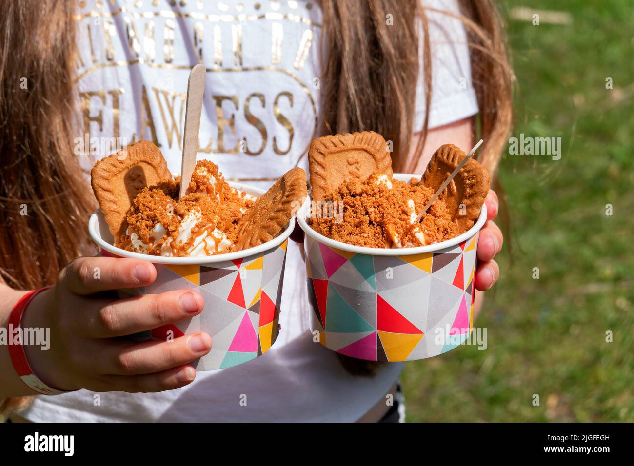 Une jeune fille détient deux portions de la glace Biscoff. La crème glacée est servie avec des biscuits Biscoff entiers et émietlés ainsi que de la pâte Biscoff. Banque D'Images