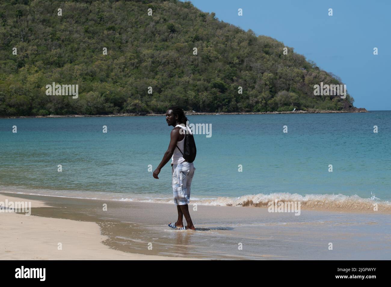 Rodney Bay, Sainte-Lucie - 27 mars 2022 - Un vendeur de plage se promène à travers les vagues sur l'idyllique plage de Reduit Banque D'Images