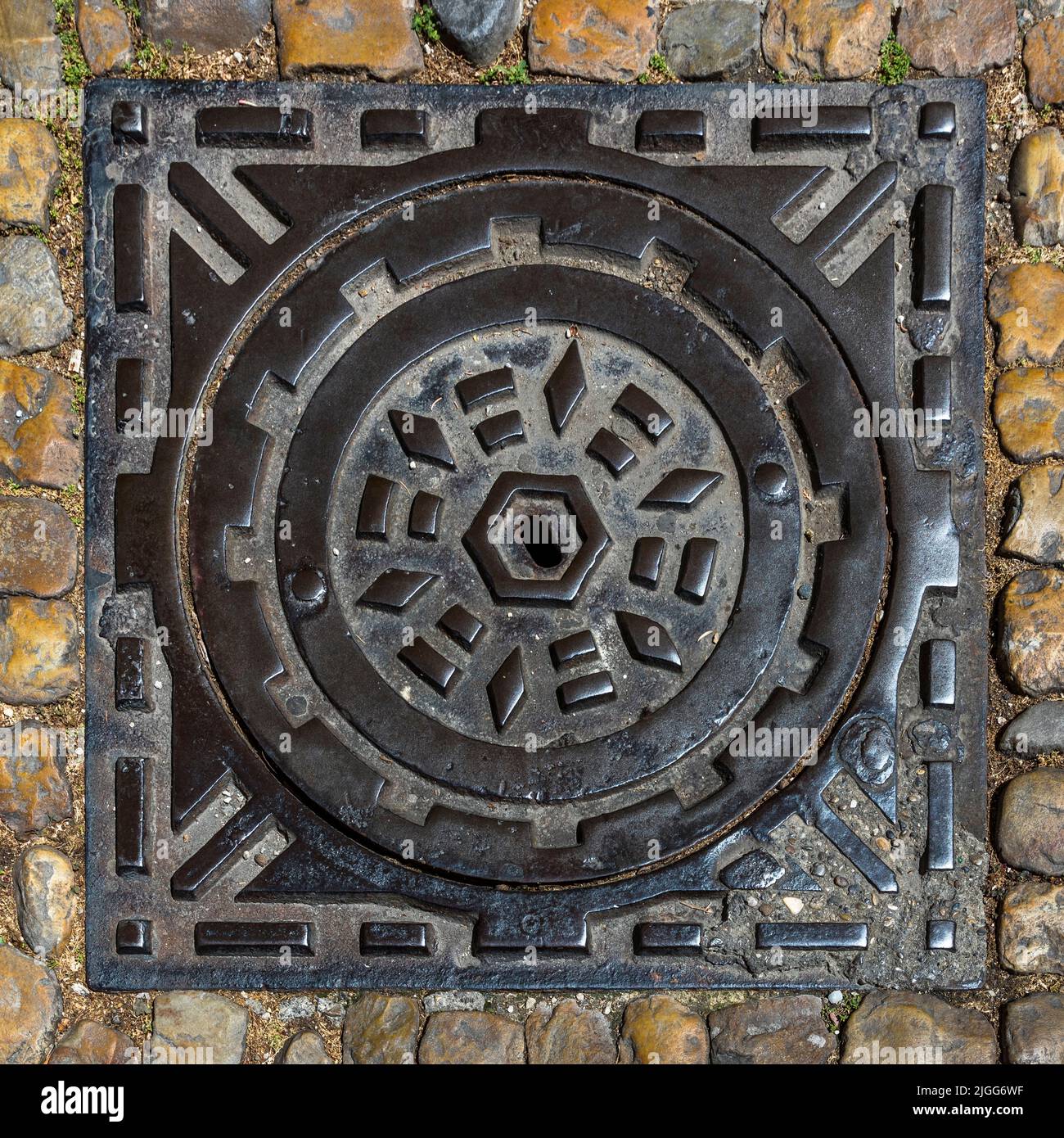 Un couvercle d'égout en fonte à motifs ornés gît sur les pavés d'une ruelle à Avignon, en France. Des cercles concentriques et des formes en losange ornent la plaque ronde. Banque D'Images