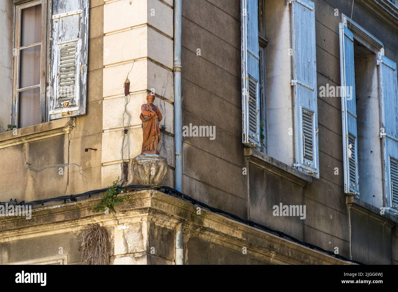 Une statue érodée d'un saint se dresse dans une niche au coin de la façade d'un bâtiment à Avignon, en France, flanquée de deux volets peints en bleu. Banque D'Images
