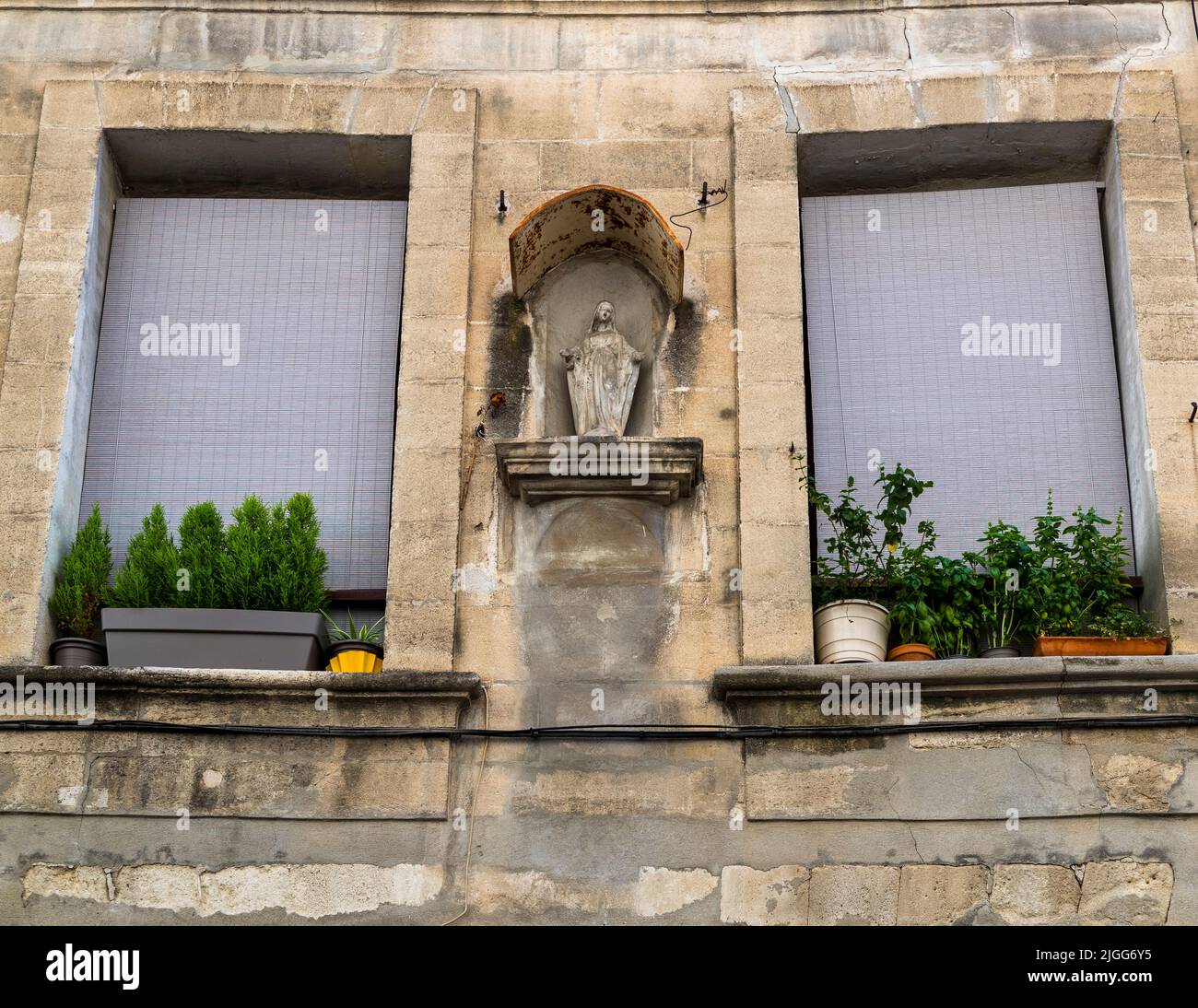 Une statue de la Vierge Marie se dresse dans une niche entre deux appuis de fenêtre bordés de pots d'herbes sur une façade de maison sur la Place Carnot à Avignon, en France. Les figures de la Madone comme celle-ci sont typiques des façades de la ville papale. Banque D'Images