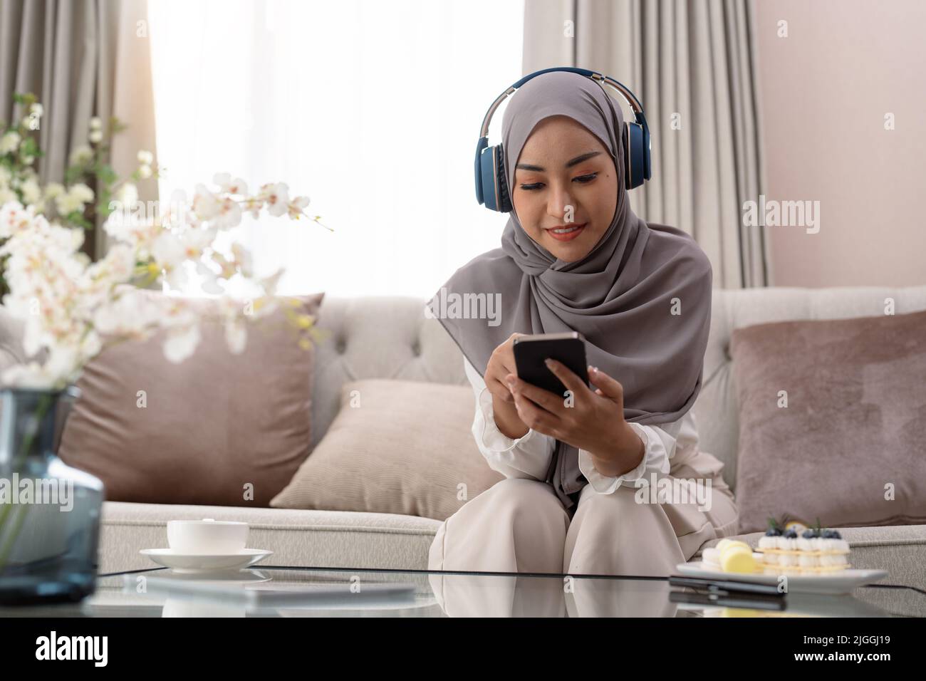 Portrait d'une jolie femme musulmane dans le hijab et casque à l'écoute de la musique à la maison. femme asiatique dans le foulard arabe appréciant un livre audio intéressant ou agréable Banque D'Images