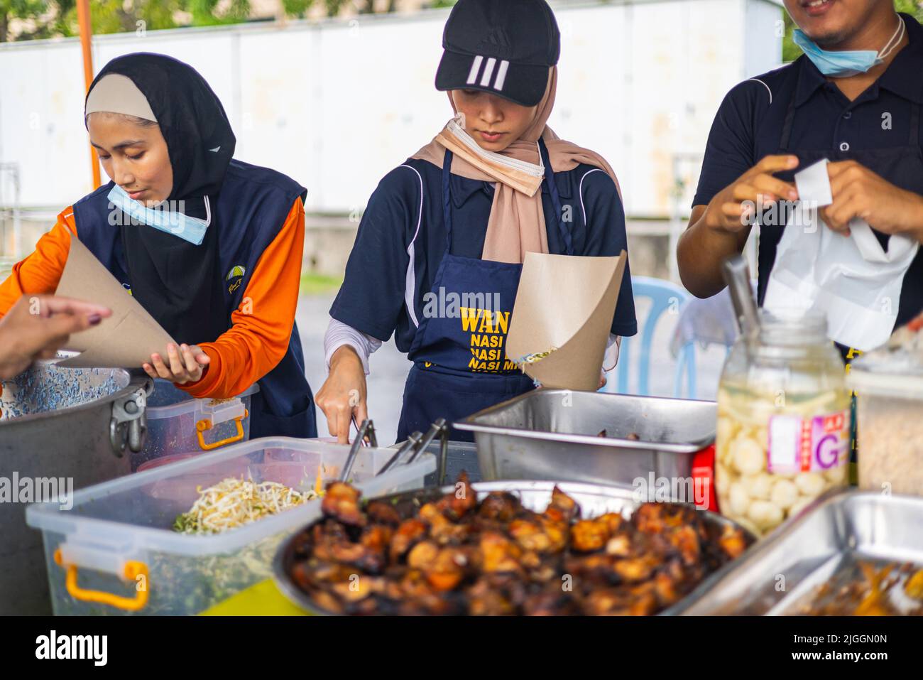 Kuala Lumpur, Malaisie - 21 juin 2022: Jeunes filles vendant du poulet barbecue sur un marché de rue. Le poulet grillé mariné est mis dans un sac de papier par deux te Banque D'Images