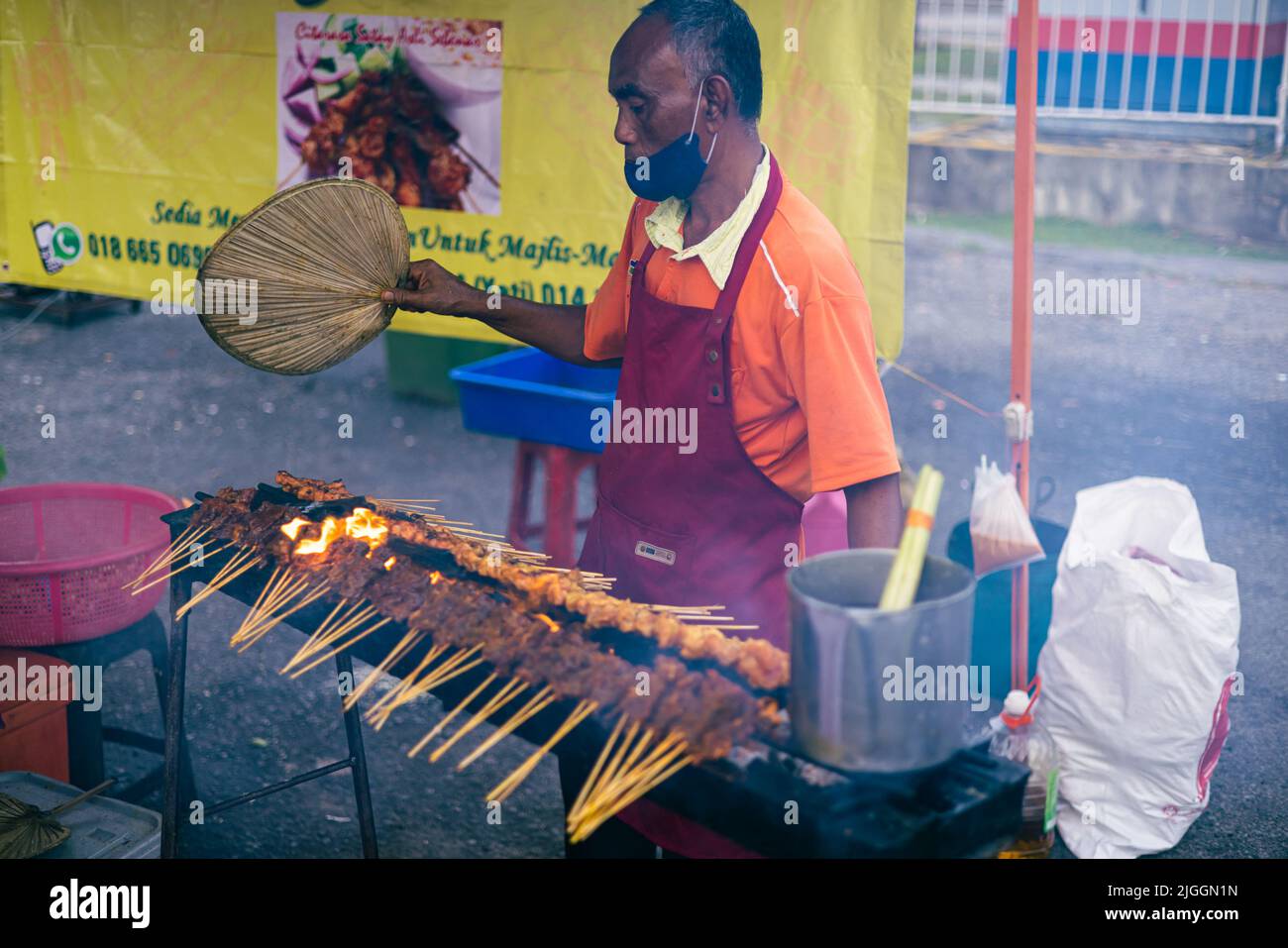 Kuala Lumpur, Malaisie - 21 juin 2022 : les barbecues de vieux hommes sont en feu ouvert sur un marché de nuit. Le plat sate est un plat grillé originaire d'Indonésie mais il est très bon Banque D'Images