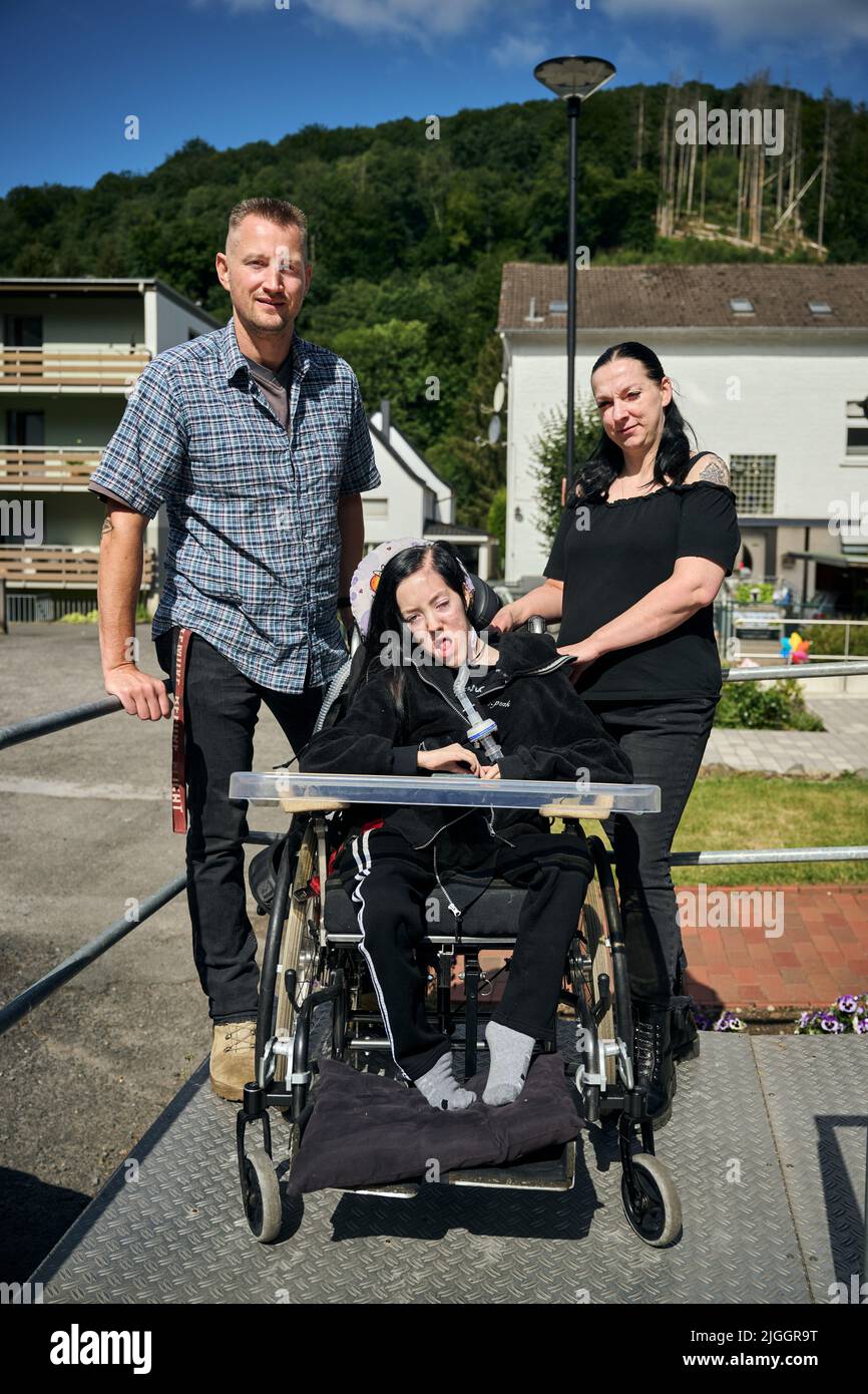 PRODUCTION - 08 juillet 2022, Rhénanie-du-Nord-Westphalie, Hagen: Dustin Raatz se trouve à côté du fauteuil roulant de Chantal et de sa mère Bianca Caspari devant leur maison. Raatz avait secouru la jeune fille gravement malade lors des graves inondations de l'année dernière avec un véhicule de l'armée allemande pesant plusieurs tonnes du musée et l'avait mise en sécurité après que la dernière batterie de son respirateur ait été presque vide. Ce mardi, il recevra la médaille de sauvetage de l'État du NRW par le ministre-président Hendrik Wüst (CDU) pour ses efforts courageux et altruistes. (À dpa : un conducteur de grue sauve une fille de l'inondation - avec vehi Banque D'Images