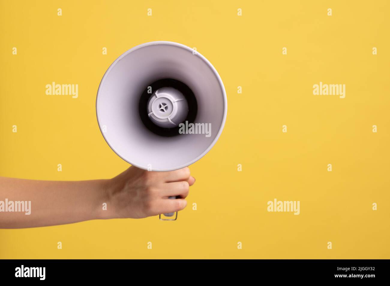 Vue de profil de la femme tenant le mégaphone à la main, haut-parleur pour annoncer la publicité. Studio d'intérieur isolé sur fond jaune. Banque D'Images