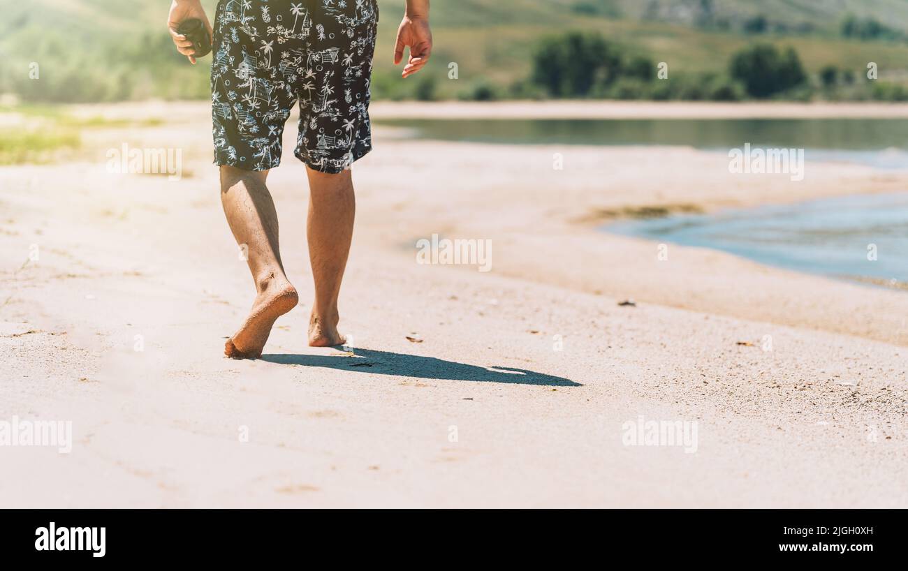 Homme en short marchant sur la plage de sable Banque D'Images