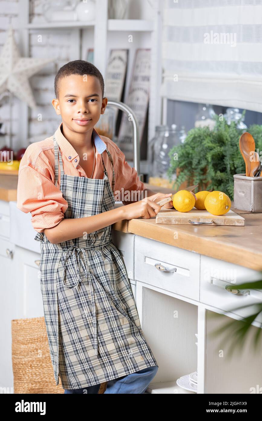 Enfant noir cuisant du citron frais dans la cuisine à la maison. Enfant africain se préparant sur la table. Banque D'Images