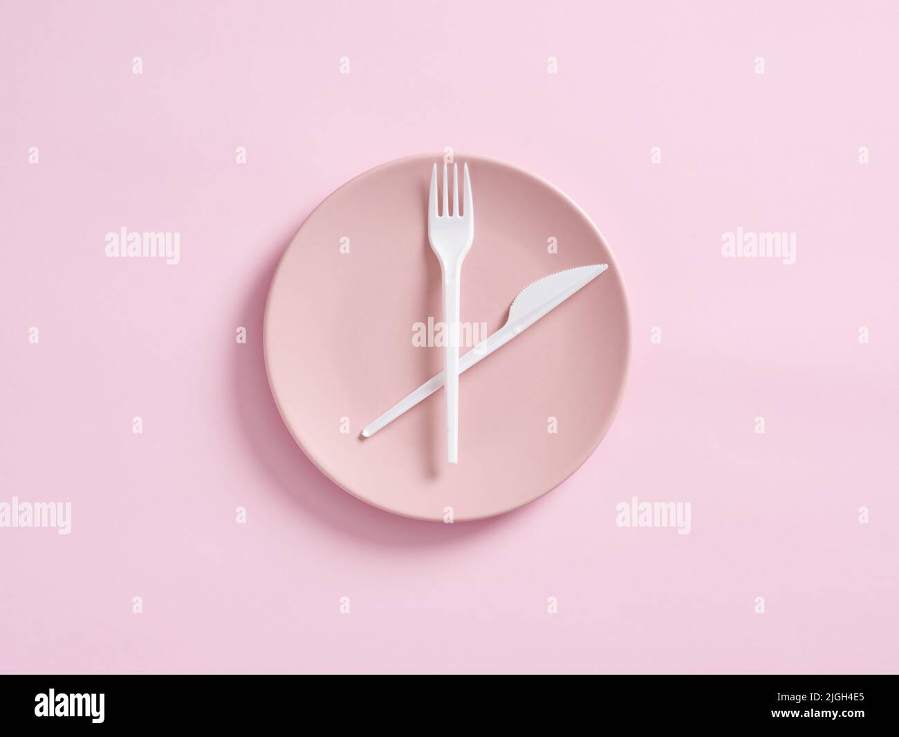 Couteau et fourchette sur plaque rose conçu comme horloge. Jeûne intermittent, déjeuner, perte de poids, plan de repas ou concept de régime. Banque D'Images