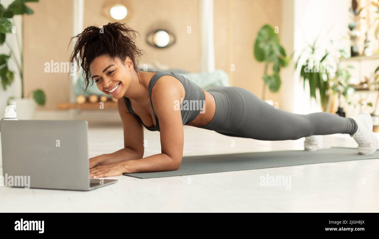 FIT afro-américaine femme planking devant un ordinateur portable, entraînement à la maison, regarder des cours de fitness en ligne, panorama Banque D'Images