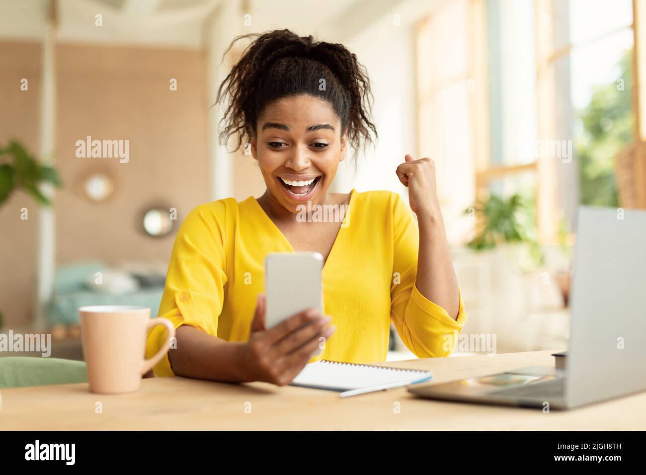 Femme afro-américaine excitée regardant l'écran de smartphone et gestant OUI, se sentant heureuse à la maison Banque D'Images