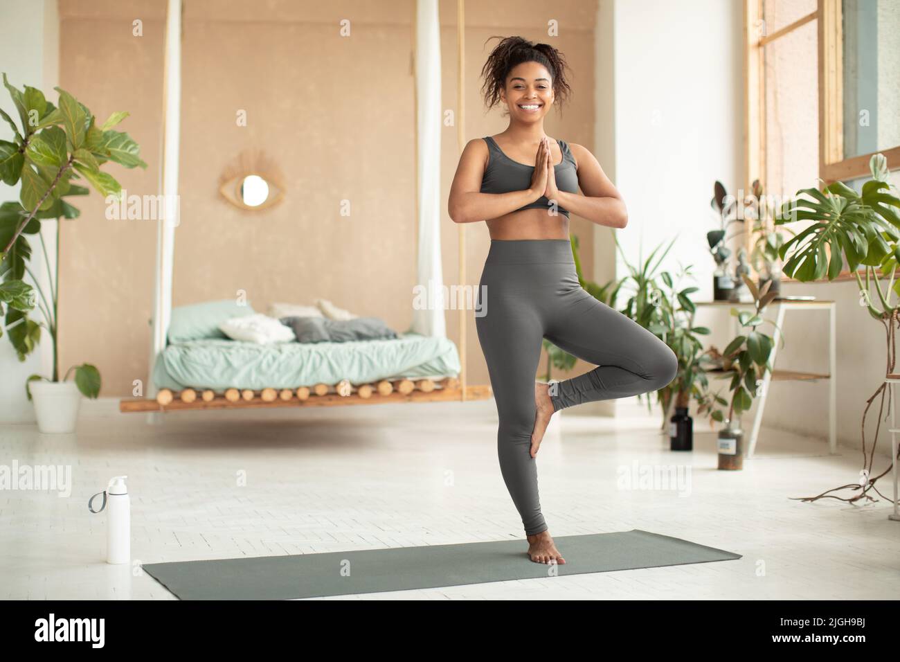 Équilibre de vie. Bonne dame noire pratiquant le yoga, faisant poser un arbre, s'entraîner sur un tapis de fitness à la maison, copier l'espace Banque D'Images