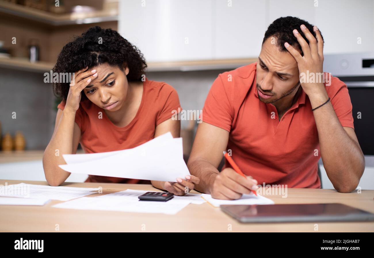 Une jeune femme et un mari afro-américains triste et désespérés travaillent avec des documents, paient des taxes sur l'intérieur de la cuisine Banque D'Images