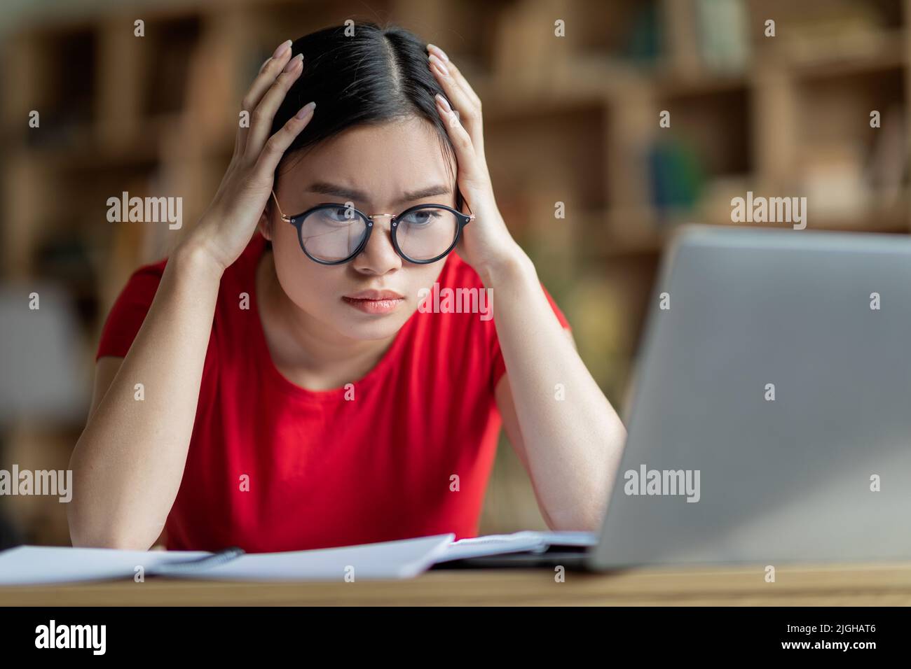 Concentrée occupé jeune fille asiatique dans les lunettes tenir la tête avec les mains, regarder l'ordinateur dans l'intérieur de la chambre Banque D'Images