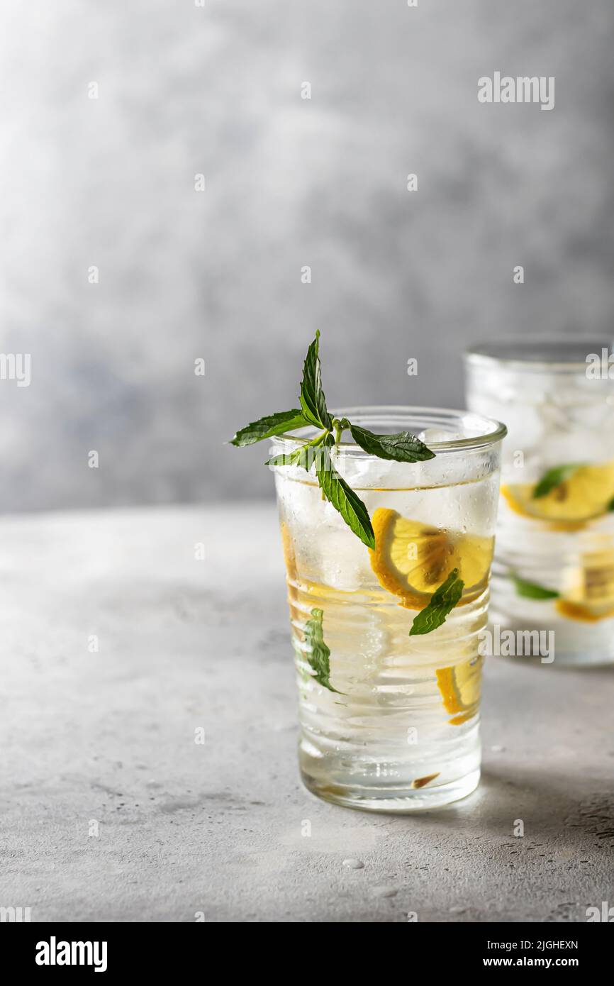 Deux verres de limonade fraîche d'été avec citron et menthe sur fond gris avec espace de texte sur la gauche. Orientation verticale Banque D'Images