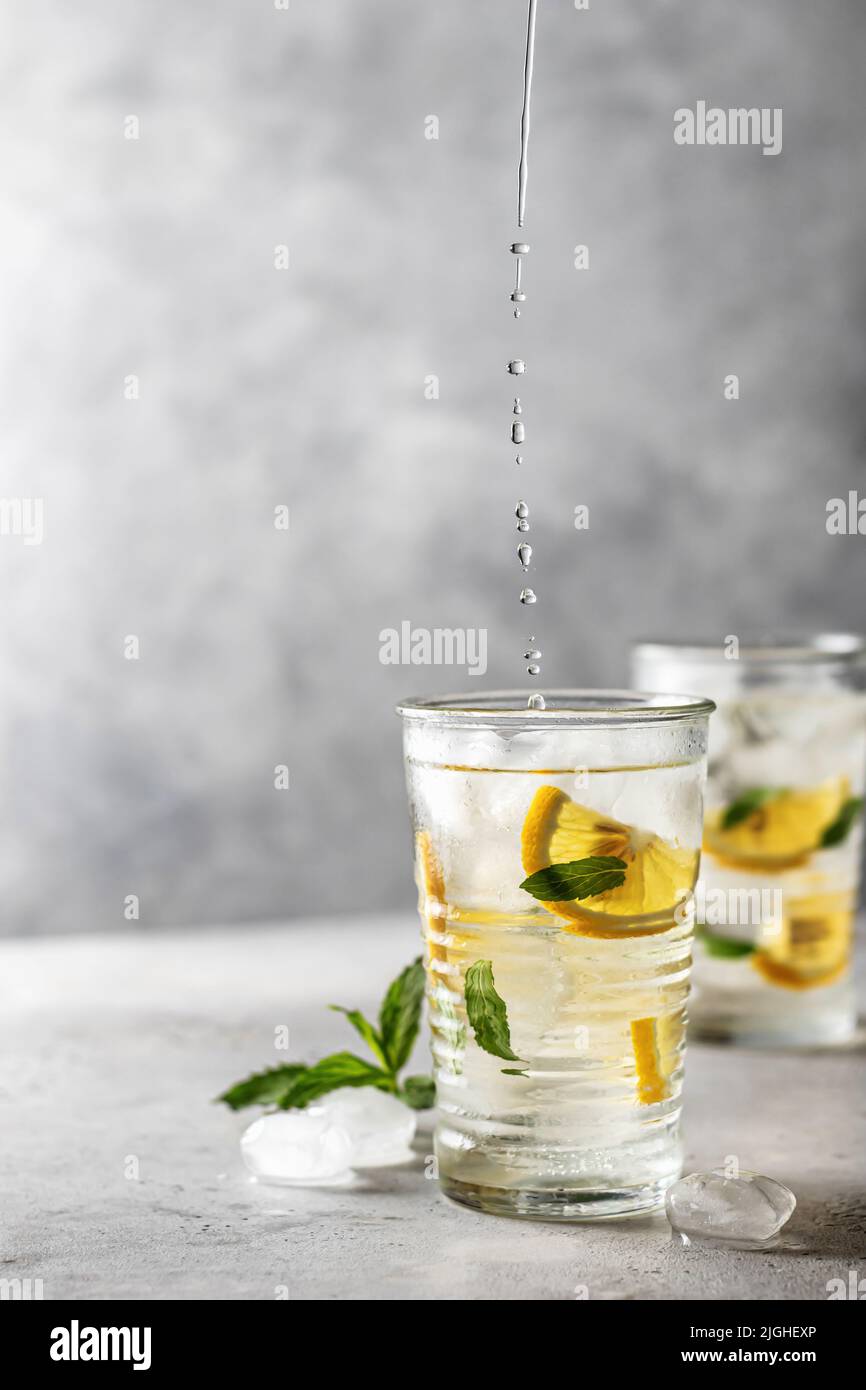 Deux verres de limonade à boisson rafraîchissante glacée d'été avec citron, menthe et glaçons sur fond gris avec espace de texte sur la gauche. Orientation verticale Banque D'Images
