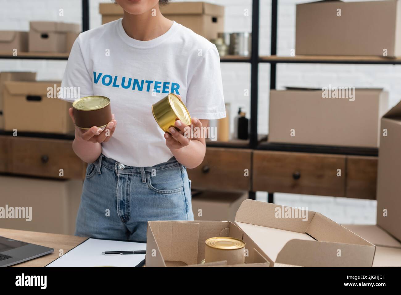 vue rognée d'une femme afro-américaine qui tient des aliments en conserve tout en travaillant dans un entrepôt de dons Banque D'Images