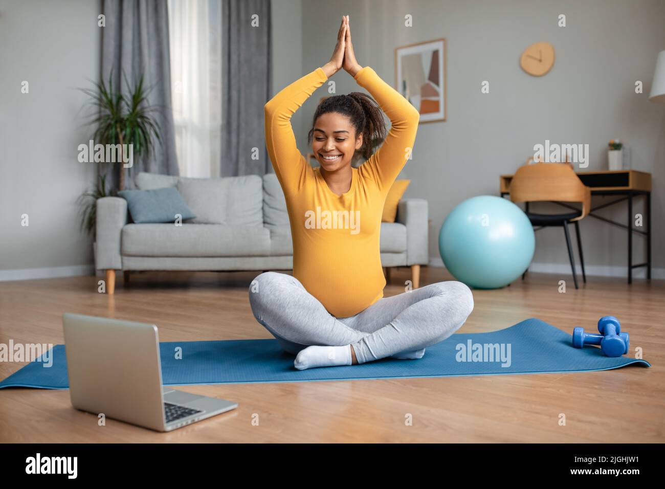 Bonne jeune femme enceinte noire avec grand ventre s'assoit dans la position de lotus pratiques de yoga et de montres entraînement vidéo Banque D'Images