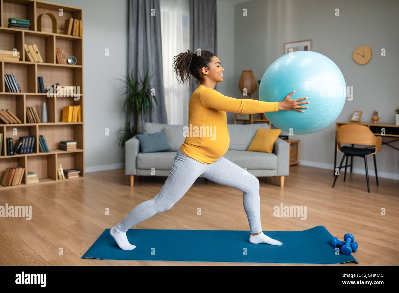 Souriant jolie jeune femme enceinte noire faisant des exercices avec le ballon de fitness sur le tapis, profiter de la maternité Banque D'Images