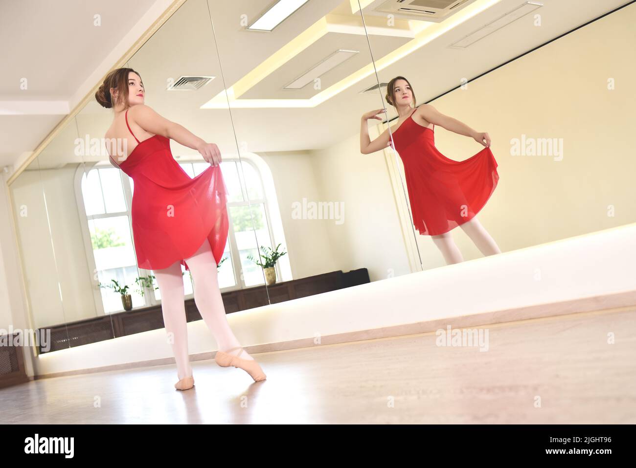 une jeune ballerine en robe rouge et des chaussures pointe effectuent des exercices dans un studio de danse Banque D'Images