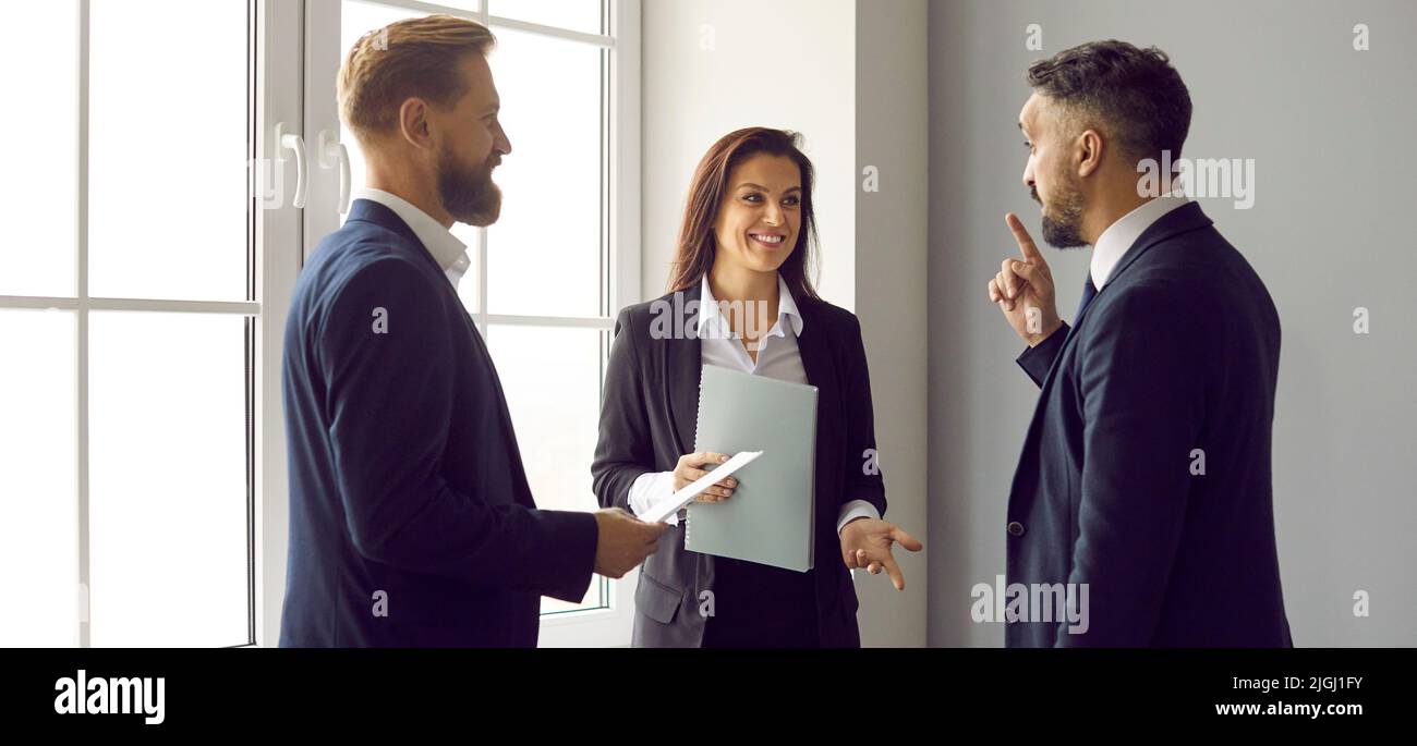 Groupe de gens d'affaires heureux debout près de la fenêtre du bureau et ayant une discussion Banque D'Images