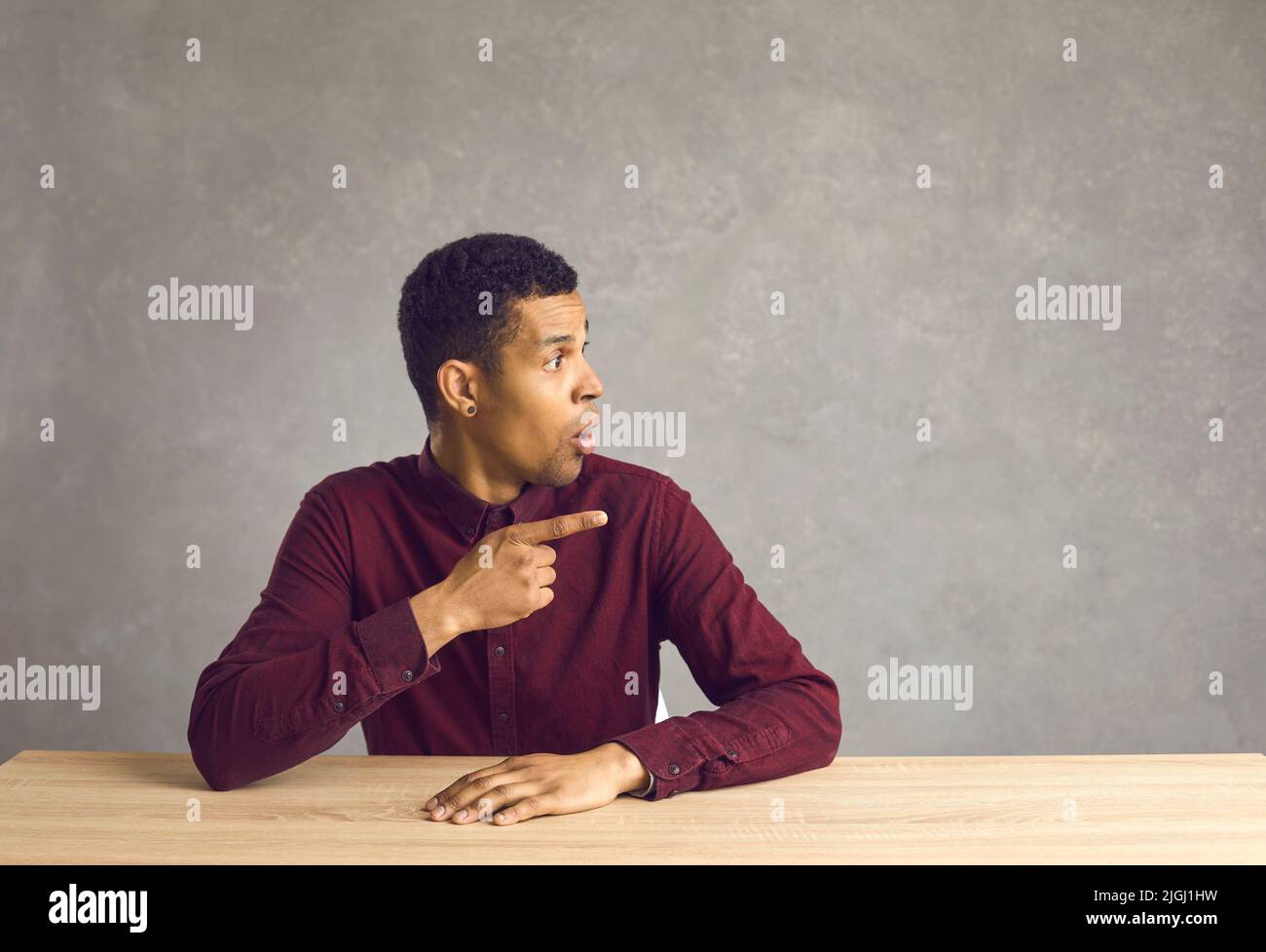 Surpris jeune homme noir assis au bureau regardant et pointant vers l'arrière-plan de l'espace de copie Banque D'Images