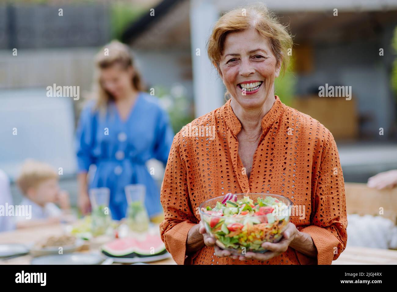 Bonne femme senior qui sert de la salade lors de la fête de jardin de plusieurs générations en été. Banque D'Images