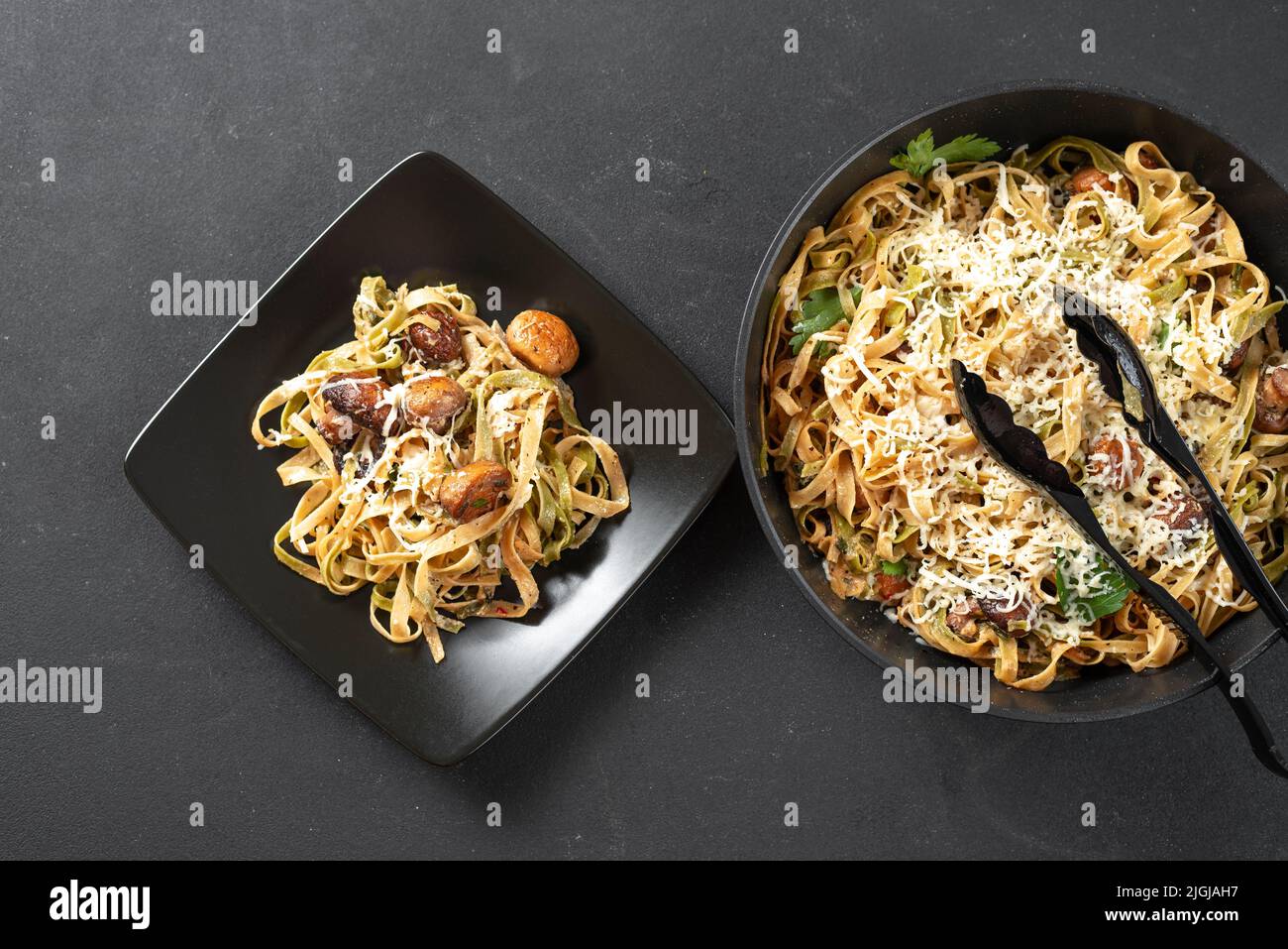 pâtes alfredo aux champignons dans une sauce à la crème sur une assiette noire sur fond sombre. Pâtes fraîchement cuites dans une poêle en fonte. À côté de la plaque avec Banque D'Images