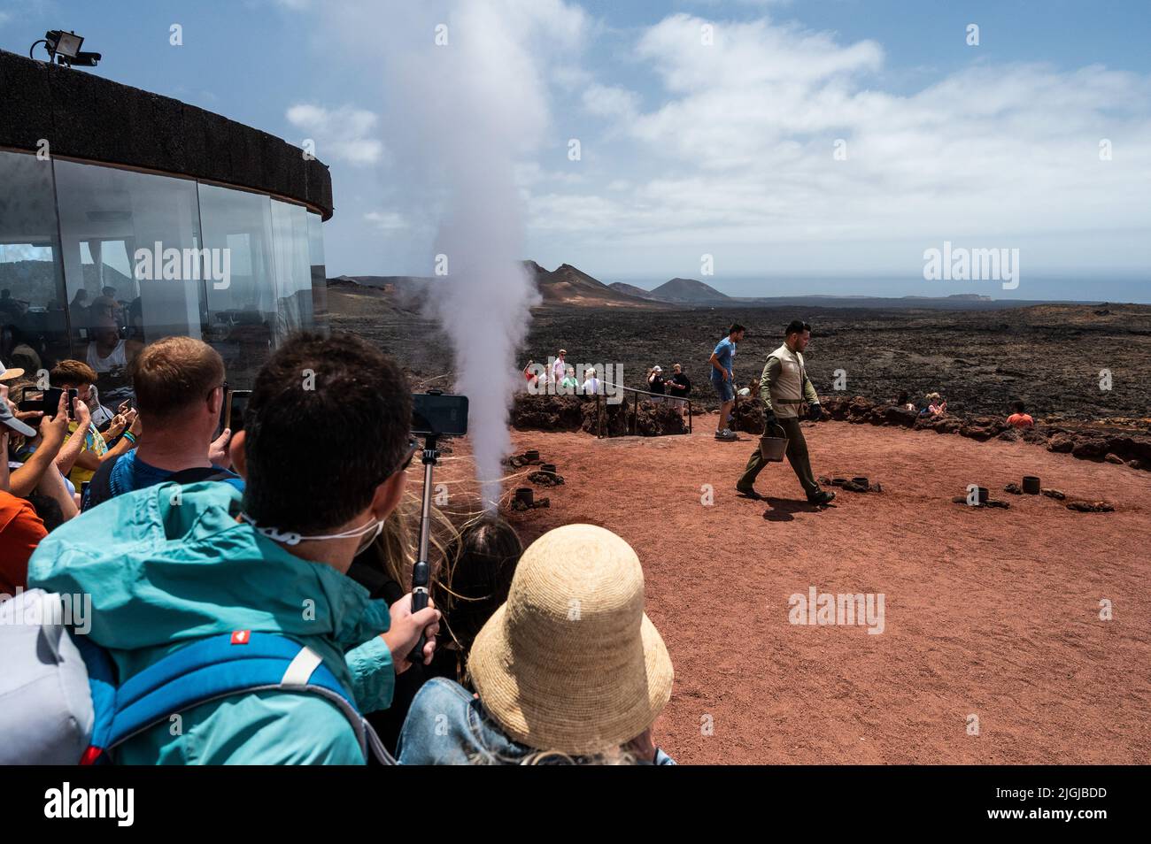 Un travailleur montre aux visiteurs un grand jet de vapeur d'eau produit en versant de l'eau dans un conduit dans le sol sous une zone volcanique à haute température dans Banque D'Images