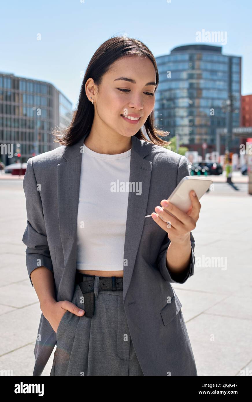 Une jeune femme d'affaires asiatique porte un costume debout dans la rue en utilisant le téléphone. Banque D'Images