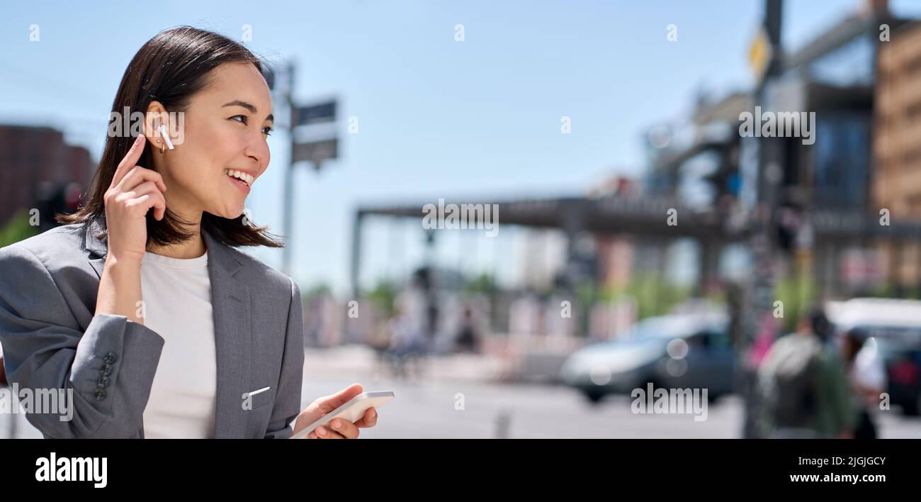 Jeune femme asiatique parlant au téléphone avec des écouteurs sans fil dans la rue de la ville. Banque D'Images