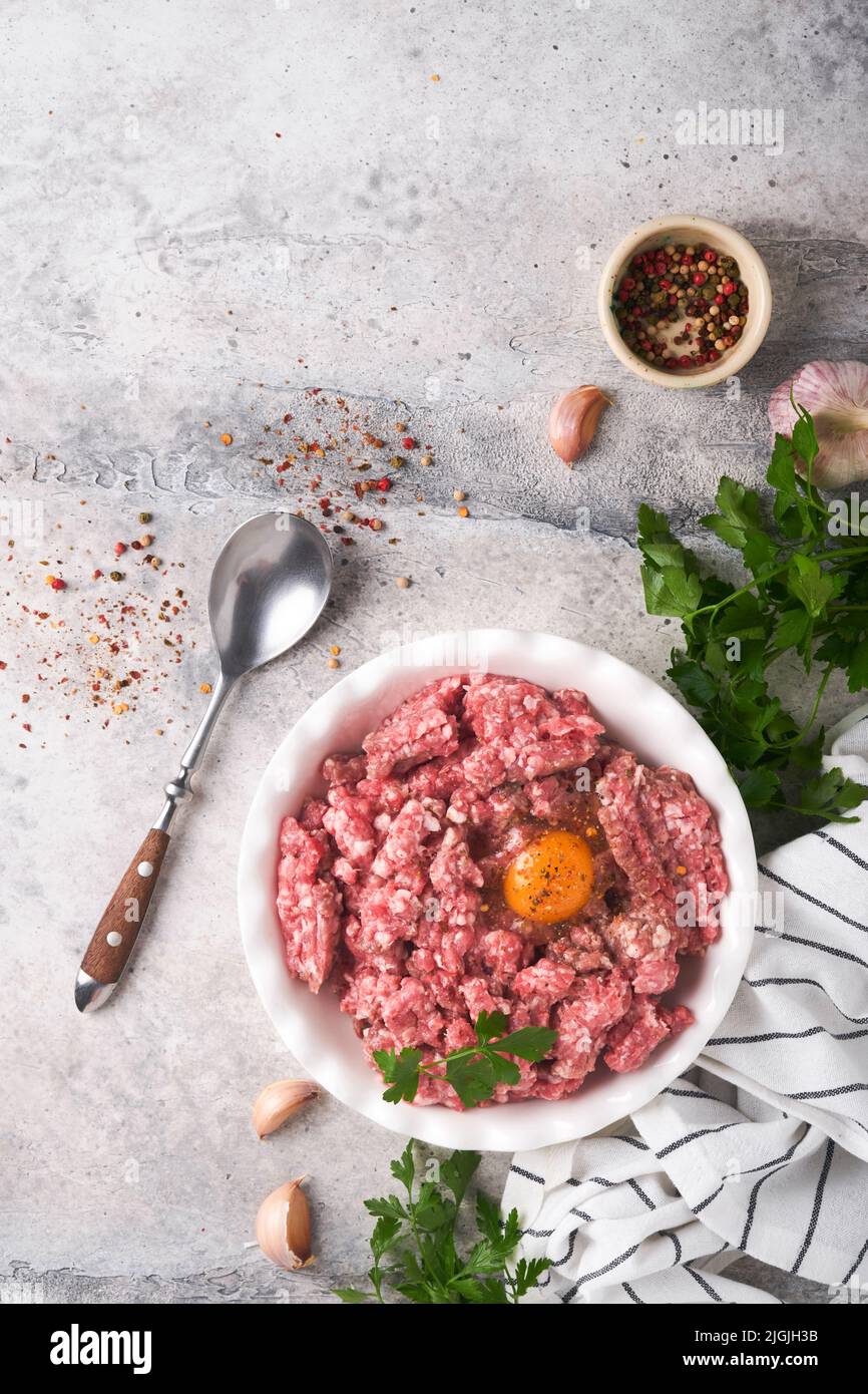Viande hachée crue. Viande hachée de bœuf, porc ou épices d'agneau, herbes et œufs sur plaque blanche sur fond de béton gris clair. Viande fraîche hachée prête pour c Banque D'Images Viande hachée crue. Viande hachée de bœuf, porc ou épices d'agneau, herbes et œufs sur plaque blanche sur fond de béton gris clair. Viande fraîche hachée prête pour c Banque D'Images