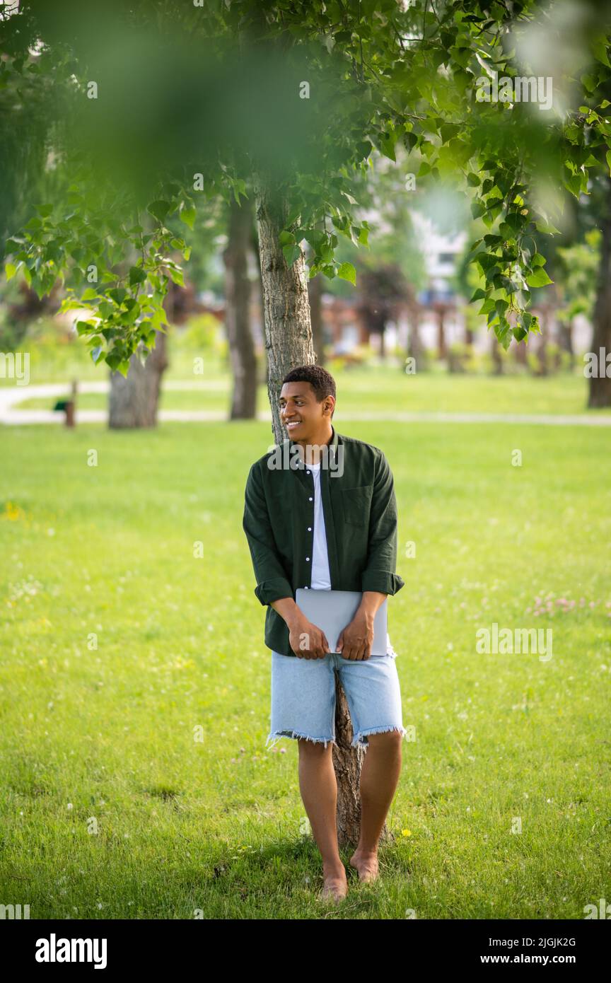 Homme avec un ordinateur portable debout contre l'arbre Banque D'Images