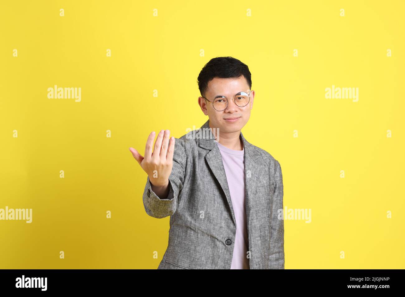 L'homme LGBTQ asiatique avec blazer gris debout sur fond jaune. Banque D'Images