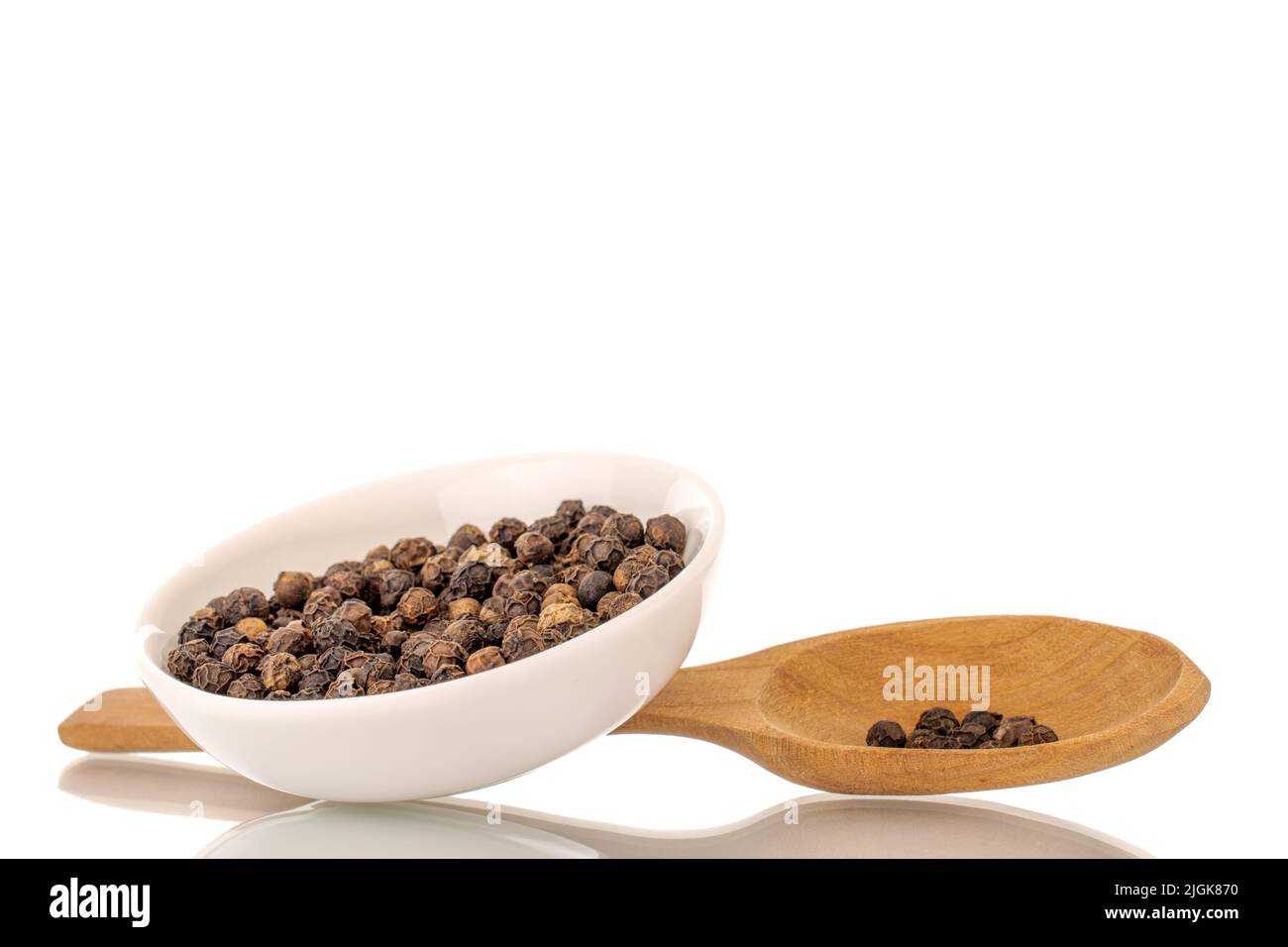 Séchez le poivre noir parfumé dans une soucoupe blanche avec une cuillère en bois, en gros plan, isolée sur un fond blanc. Banque D'Images