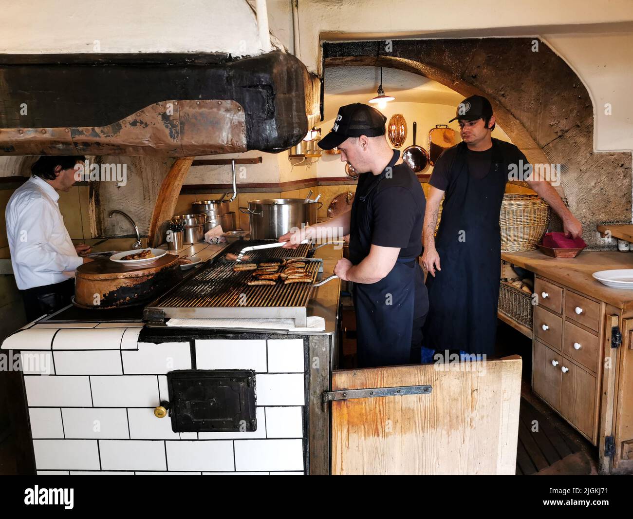 Regensburg, ALLEMAGNE - 09.17.2019: Les chefs cuisiniers cuisinent avec des saucisses allemandes traditionnelles sur le grill dans une cuisine de pub. Banque D'Images