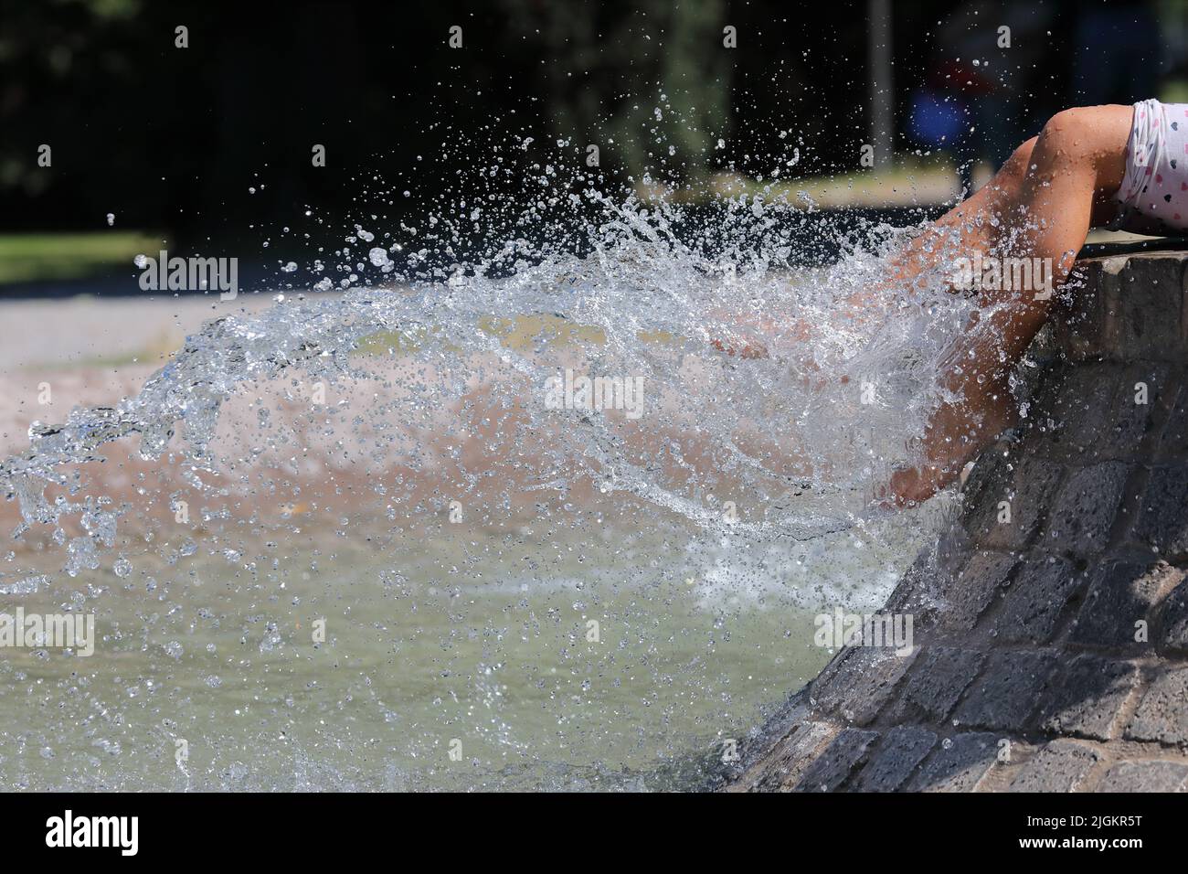 De belles jambes d'une fille assise sur une fontaine de la ville. Mise au point sélective. Des jets d'eau fraîche laver les pieds des femmes lors d'une chaude journée d'été. Banque D'Images