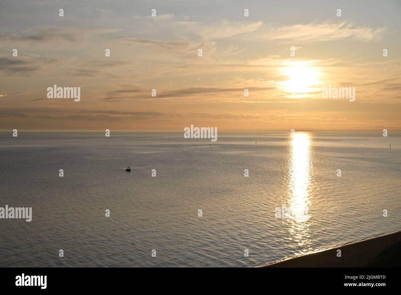 Coucher de soleil sur les eaux calmes et étincelantes de la baie de Port Phillip, avec des nuages lumineux dans le ciel, tandis qu'un petit bateau se dirige vers la rive Banque D'Images