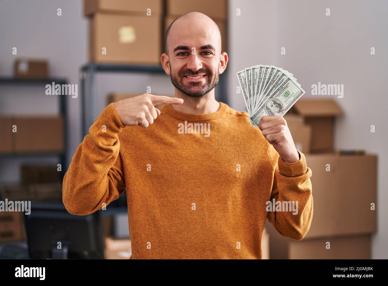 Jeune homme chauve avec la barbe de travail à la petite entreprise ecommerce tenant l'argent souriant heureux pointant avec la main et le doigt Banque D'Images