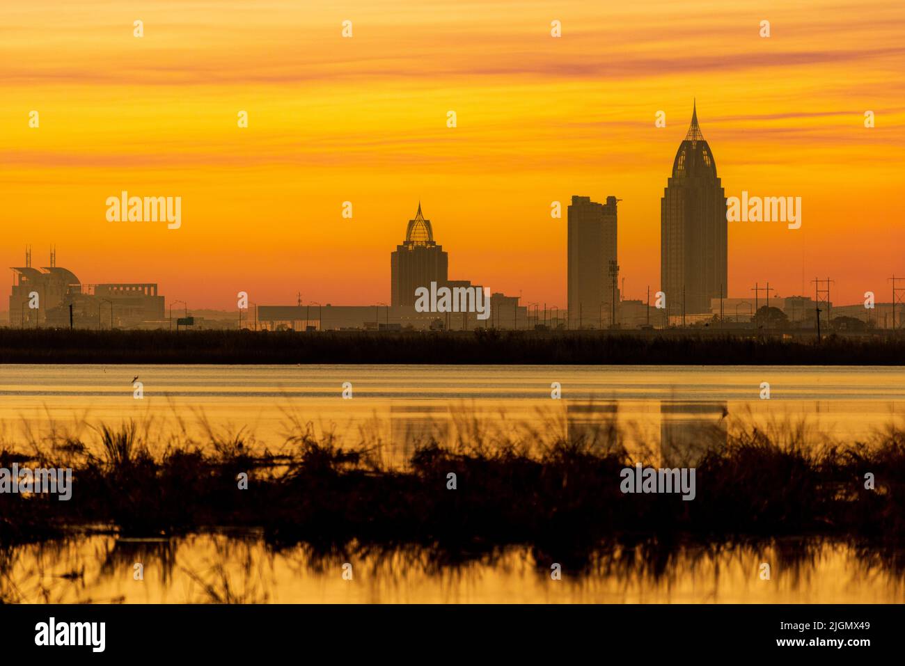 Le soleil couchant peint le ciel au-delà de la ligne d'horizon de Mobile, Alabama, comme vu de l'autre côté de Mobile Bay dans une image composite. Banque D'Images