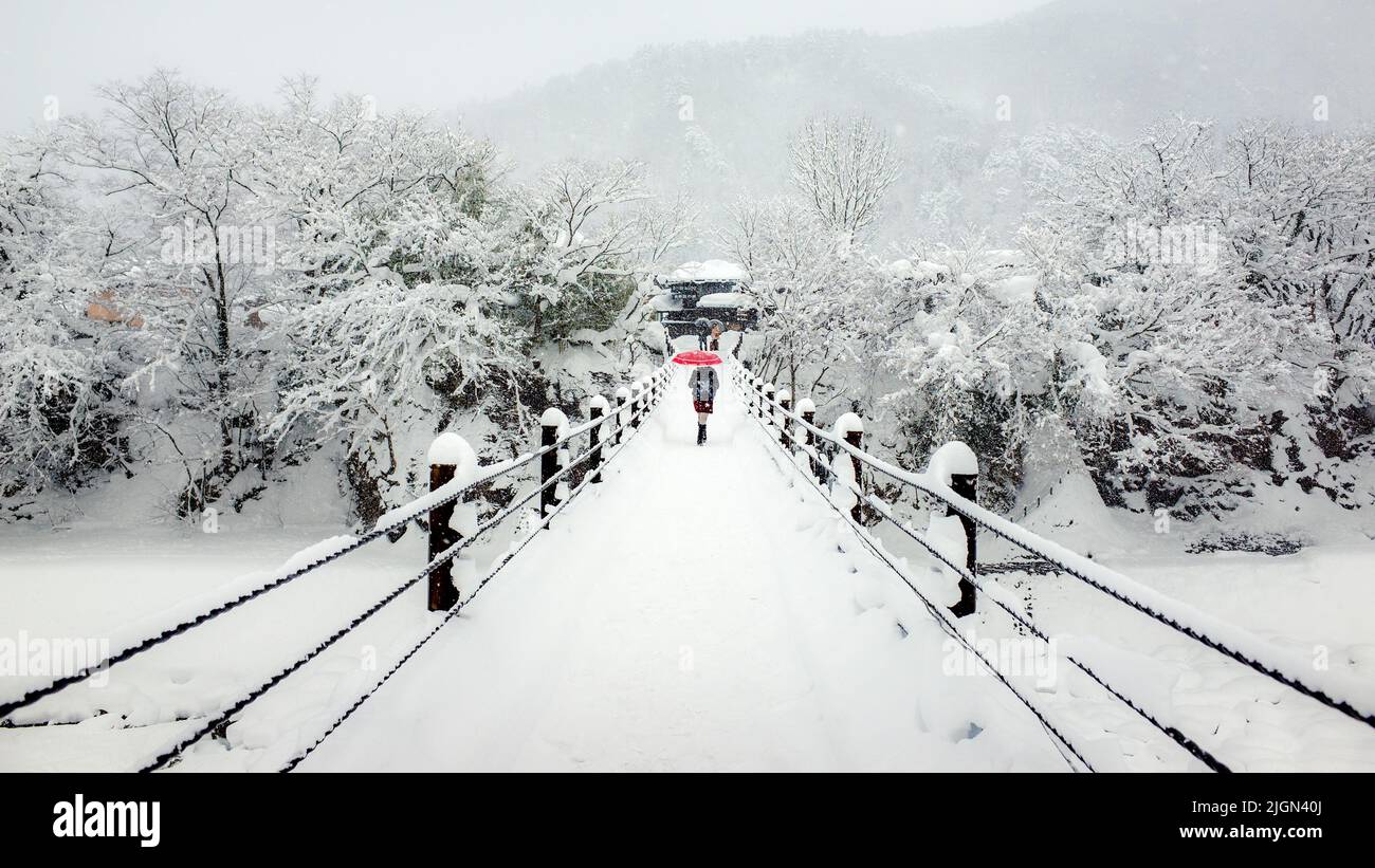 un parapluie rouge traversant le pont dans la neige Banque D'Images