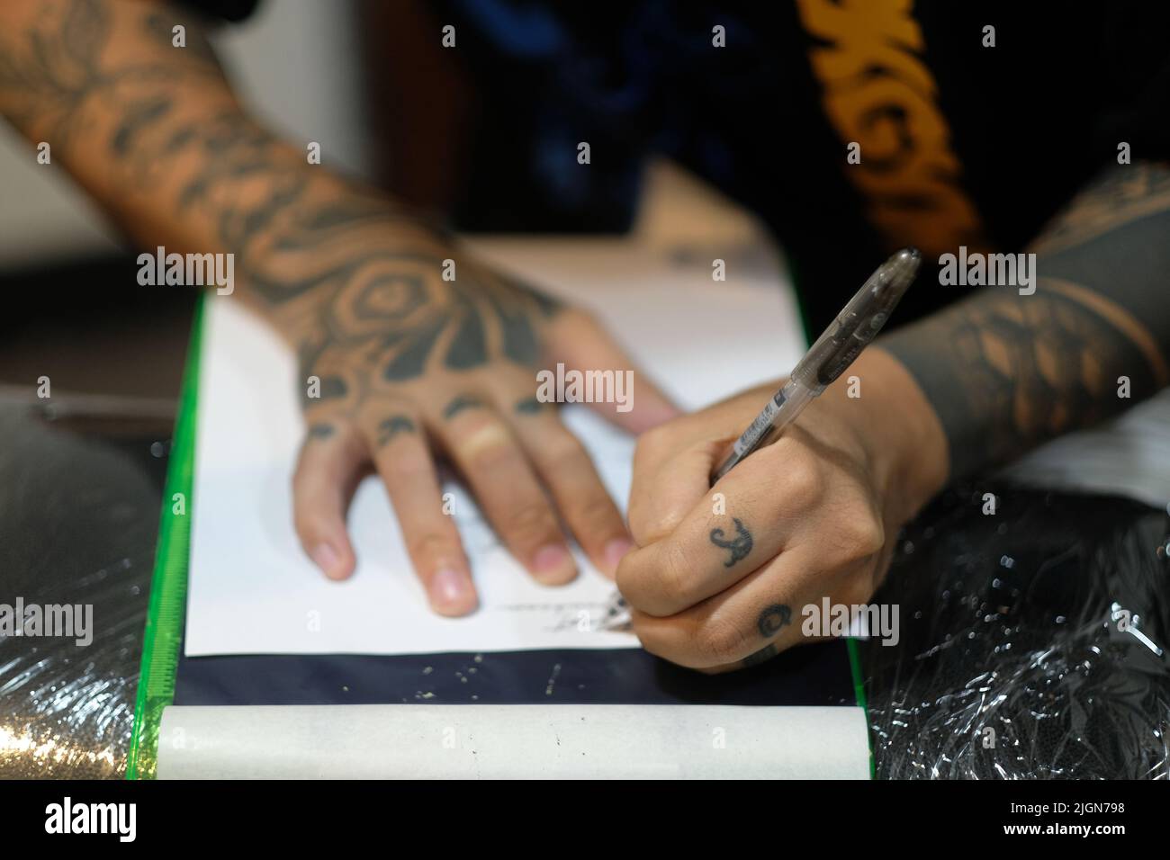 Gros plan des doigts incrustés du tatoueur alors qu'il pochoirs cursive script sur papier blanc avec un stylo en préparation pour une session de tatouage. Banque D'Images